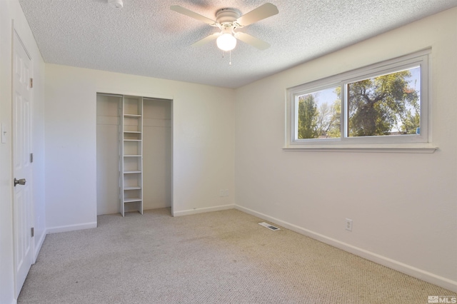 unfurnished bedroom featuring ceiling fan, a closet, light carpet, and a textured ceiling