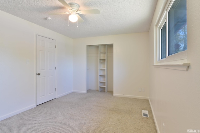 unfurnished bedroom featuring a closet, a textured ceiling, light colored carpet, and ceiling fan