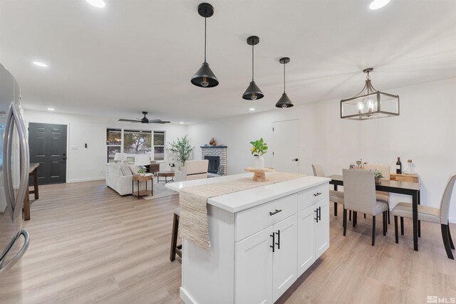 kitchen with stainless steel refrigerator, white cabinets, hanging light fixtures, and light wood-type flooring