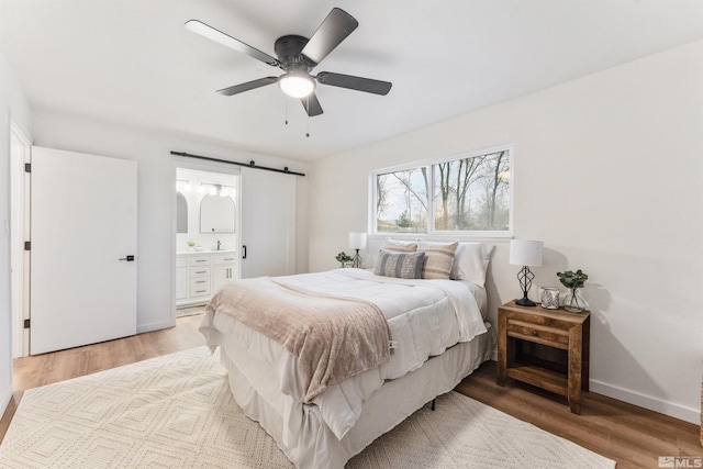 bedroom with connected bathroom, light hardwood / wood-style flooring, ceiling fan, and a barn door