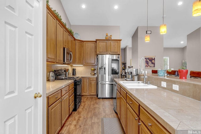 kitchen with sink, stainless steel appliances, pendant lighting, light hardwood / wood-style floors, and a kitchen island with sink