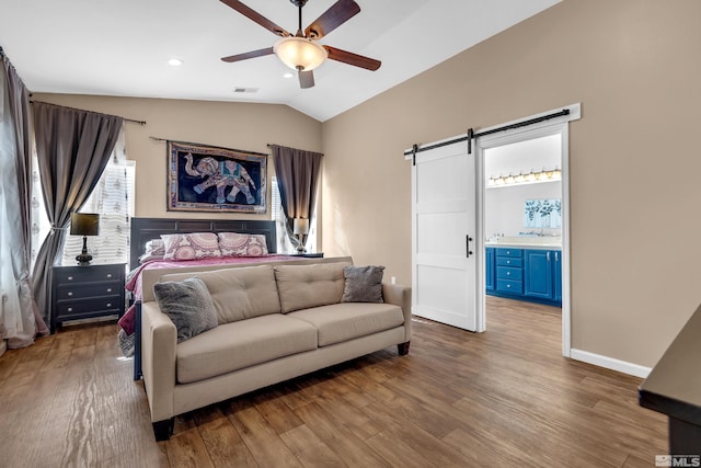 bedroom with ensuite bath, hardwood / wood-style flooring, ceiling fan, a barn door, and vaulted ceiling