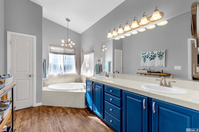 bathroom with hardwood / wood-style floors, vanity, vaulted ceiling, tiled tub, and a chandelier