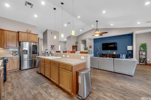 kitchen featuring hanging light fixtures, ceiling fan, an island with sink, appliances with stainless steel finishes, and wood-type flooring