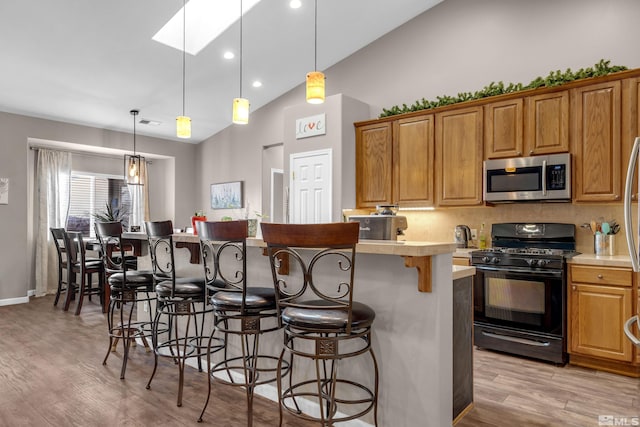 kitchen featuring light wood-type flooring, lofted ceiling with skylight, black range with gas cooktop, and hanging light fixtures