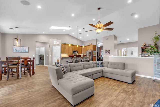 living room featuring light wood-type flooring, a skylight, ceiling fan, high vaulted ceiling, and washer / dryer