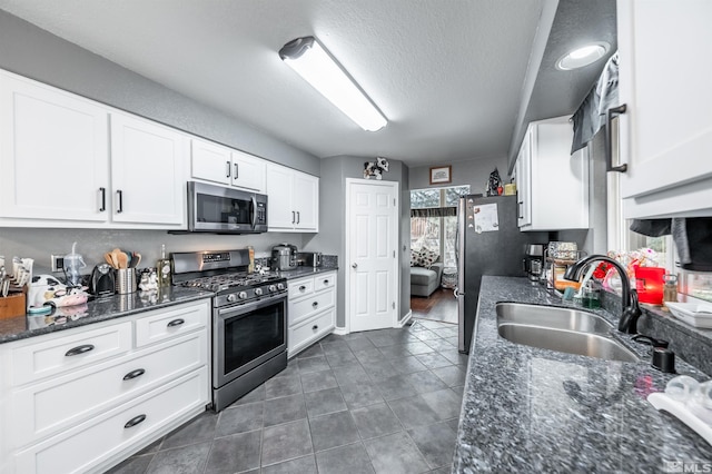 kitchen with dark stone counters, white cabinets, sink, a textured ceiling, and appliances with stainless steel finishes