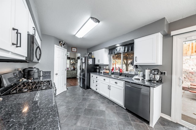 kitchen with white cabinets, stainless steel appliances, dark stone counters, and sink