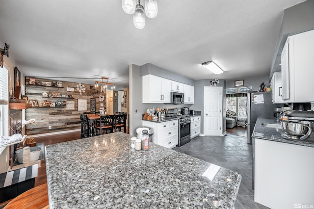 kitchen featuring dark stone counters, white cabinets, wooden walls, dark tile patterned floors, and stainless steel appliances