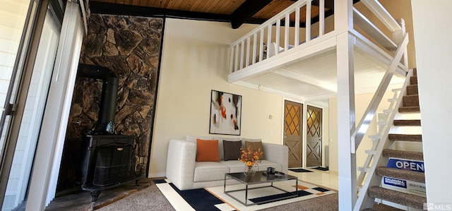 carpeted living room featuring a wood stove, beamed ceiling, and wood ceiling