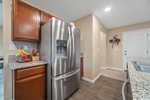 kitchen with light stone counters, dark hardwood / wood-style flooring, stainless steel refrigerator with ice dispenser, and sink