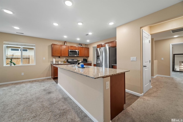 kitchen featuring light stone countertops, stainless steel appliances, light carpet, and an island with sink