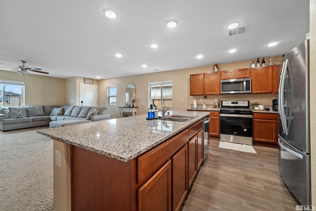 kitchen with dark wood-type flooring, a center island with sink, sink, ceiling fan, and stainless steel appliances