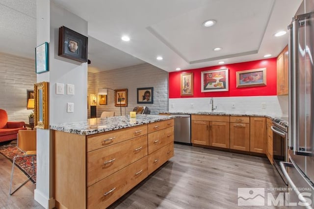 kitchen with sink, a kitchen breakfast bar, light stone counters, hardwood / wood-style floors, and appliances with stainless steel finishes