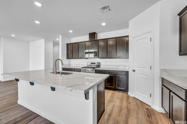 kitchen with a kitchen bar, appliances with stainless steel finishes, sink, light hardwood / wood-style flooring, and an island with sink