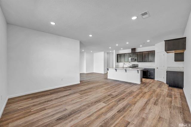 kitchen with a breakfast bar, sink, light hardwood / wood-style flooring, an island with sink, and appliances with stainless steel finishes