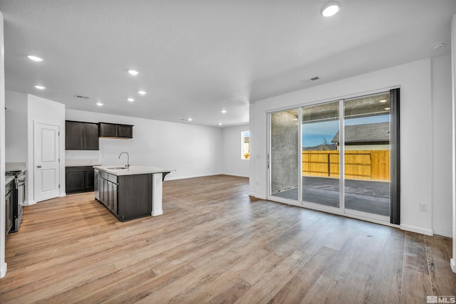 kitchen with sink, stainless steel range oven, an island with sink, light hardwood / wood-style floors, and dark brown cabinets