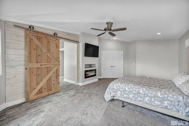 unfurnished bedroom with ceiling fan, a barn door, carpet floors, wooden walls, and a closet