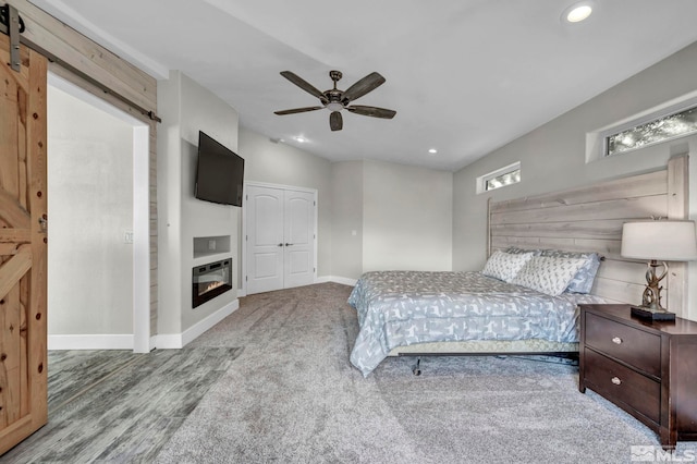 bedroom featuring a barn door, ceiling fan, a closet, and wood-type flooring