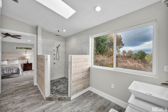 bathroom with vanity, lofted ceiling with skylight, hardwood / wood-style flooring, ceiling fan, and tiled shower