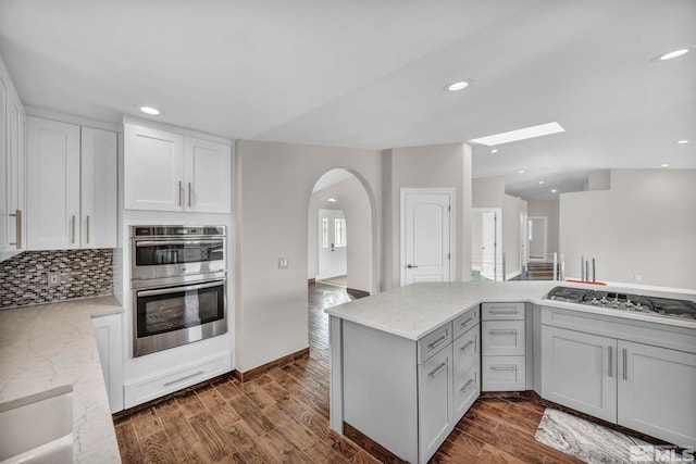 kitchen with light stone countertops, white cabinetry, stainless steel appliances, dark hardwood / wood-style floors, and decorative backsplash