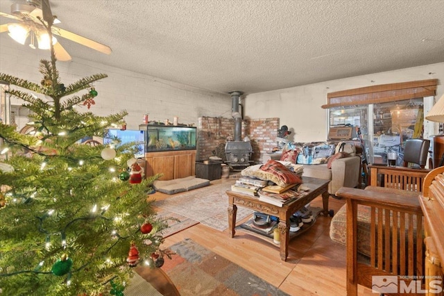 unfurnished living room featuring a wood stove, ceiling fan, hardwood / wood-style floors, and a textured ceiling