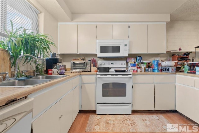 kitchen with backsplash, white appliances, sink, white cabinets, and light hardwood / wood-style floors