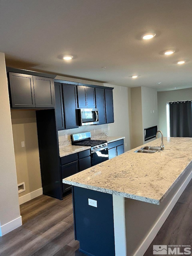 kitchen featuring light stone countertops, sink, dark hardwood / wood-style flooring, a center island with sink, and appliances with stainless steel finishes