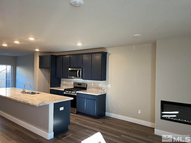 kitchen with a kitchen island with sink, sink, dark hardwood / wood-style floors, light stone countertops, and stainless steel appliances