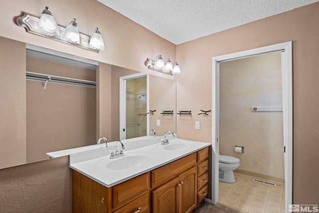 bathroom featuring vanity, toilet, a shower with door, and a textured ceiling