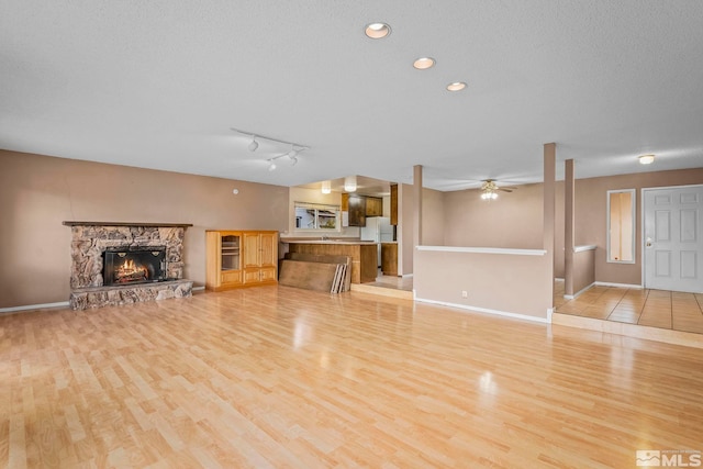 unfurnished living room featuring ceiling fan, light hardwood / wood-style floors, a stone fireplace, and a textured ceiling