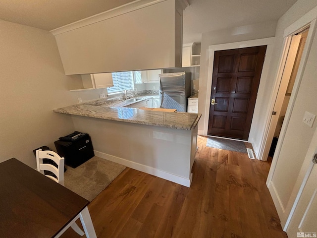 kitchen with kitchen peninsula, stainless steel fridge, white cabinets, and dark hardwood / wood-style floors