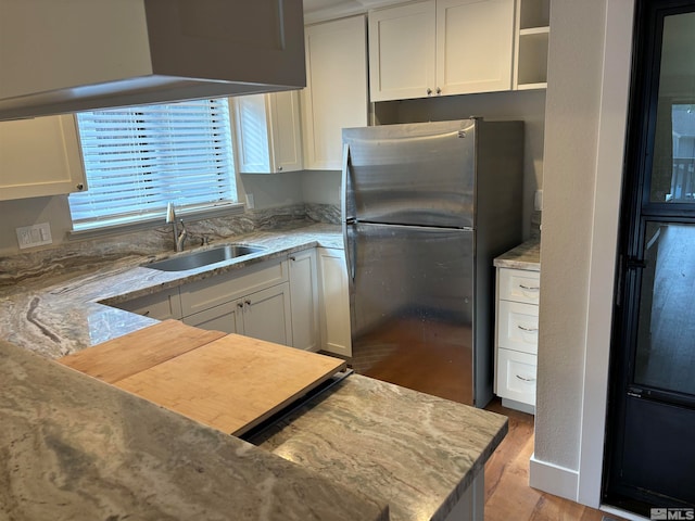 kitchen with sink, stainless steel fridge, light stone countertops, light hardwood / wood-style floors, and white cabinetry