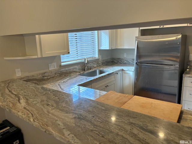 kitchen with stainless steel fridge, sink, white cabinets, and light stone countertops