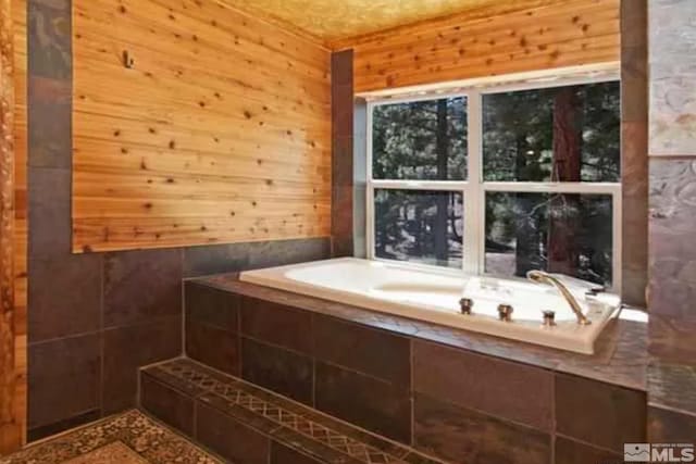 bathroom featuring tiled tub and wood walls