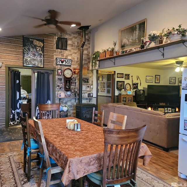 dining room featuring a wood stove, ceiling fan, and wood-type flooring