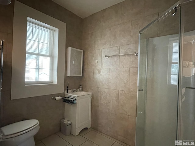 bathroom featuring tile patterned floors, plenty of natural light, a shower with shower door, and tile walls