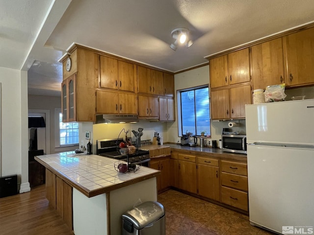 kitchen featuring tile countertops, dark wood-type flooring, a textured ceiling, appliances with stainless steel finishes, and kitchen peninsula