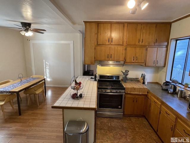 kitchen featuring kitchen peninsula, dark hardwood / wood-style flooring, gas range, ceiling fan, and tile counters