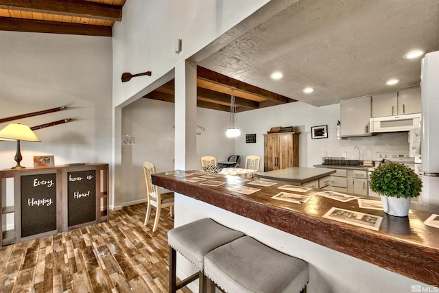 kitchen with exhaust hood, beamed ceiling, hanging light fixtures, and dark hardwood / wood-style floors