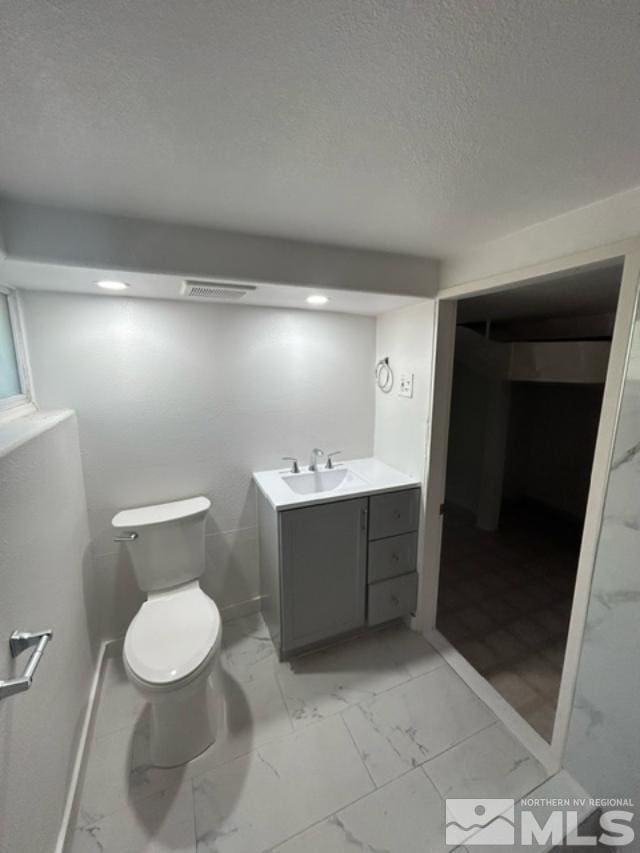 bathroom with a textured ceiling, vanity, and toilet