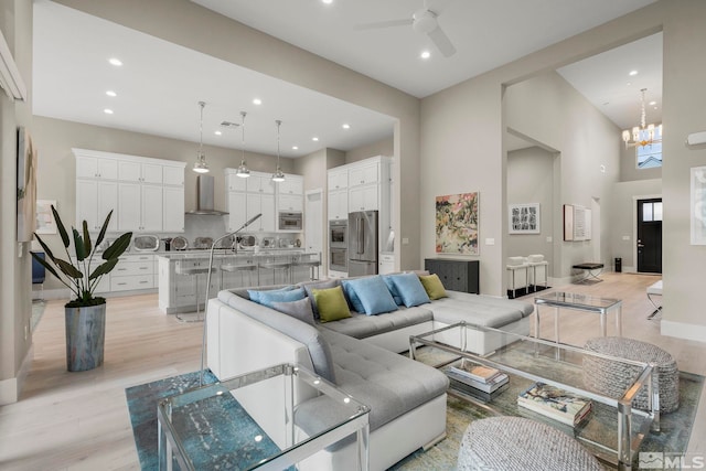 living room featuring ceiling fan with notable chandelier, light hardwood / wood-style floors, and a high ceiling