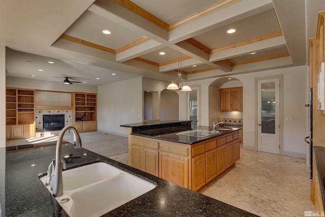 kitchen featuring ceiling fan with notable chandelier, a kitchen island with sink, electric stovetop, sink, and hanging light fixtures