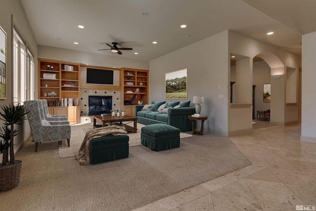 living room with a tile fireplace, built in features, and ceiling fan