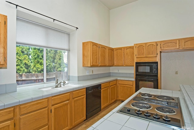 kitchen featuring a towering ceiling, sink, tile countertops, and black appliances