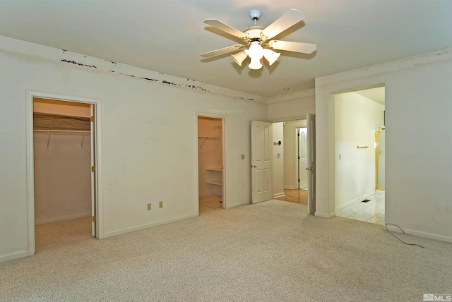 unfurnished bedroom featuring connected bathroom, ceiling fan, light colored carpet, a walk in closet, and a closet