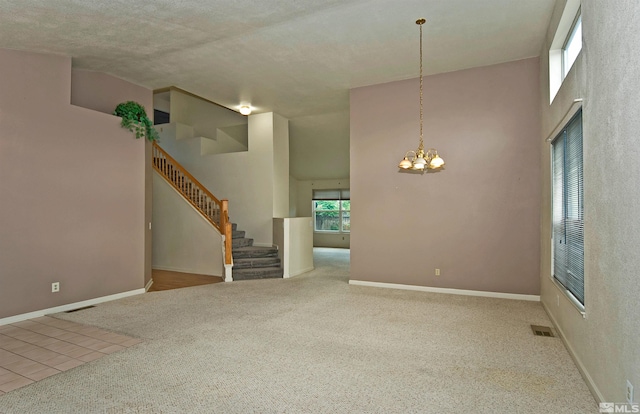 carpeted spare room with a towering ceiling, a textured ceiling, and a notable chandelier