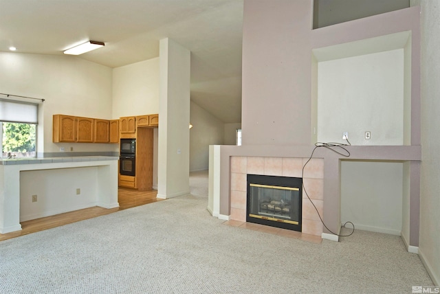 unfurnished living room with light colored carpet, high vaulted ceiling, and a tiled fireplace