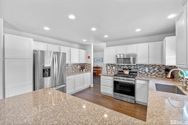 kitchen with appliances with stainless steel finishes, dark hardwood / wood-style flooring, light stone counters, sink, and white cabinets