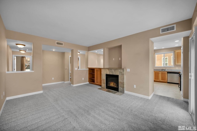 unfurnished living room with light colored carpet, baseboards, visible vents, and a tiled fireplace